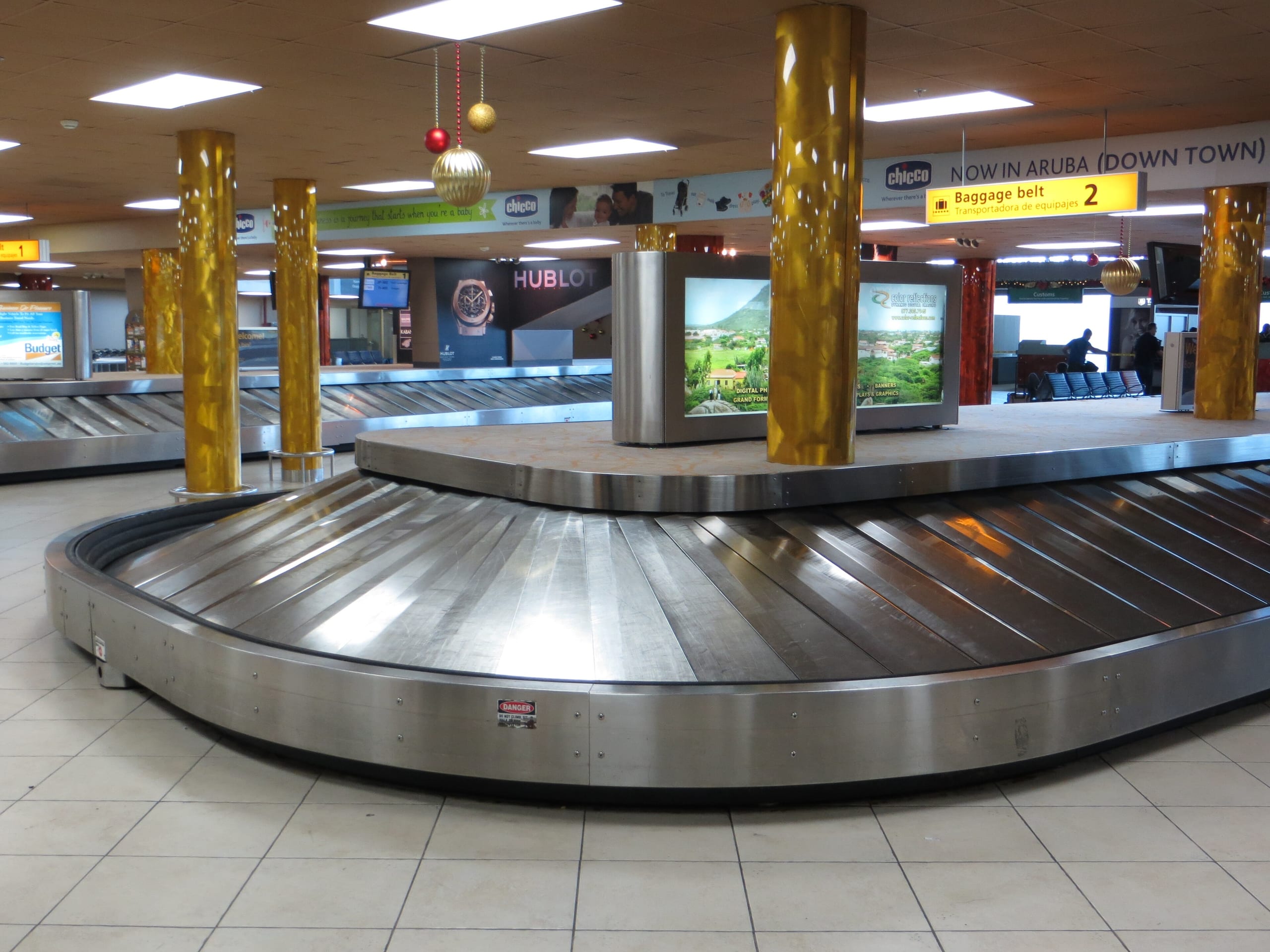 An empty baggage carousel between gold pillars in the arrivals hall at Queen Beatrix International Airport, Aruba
