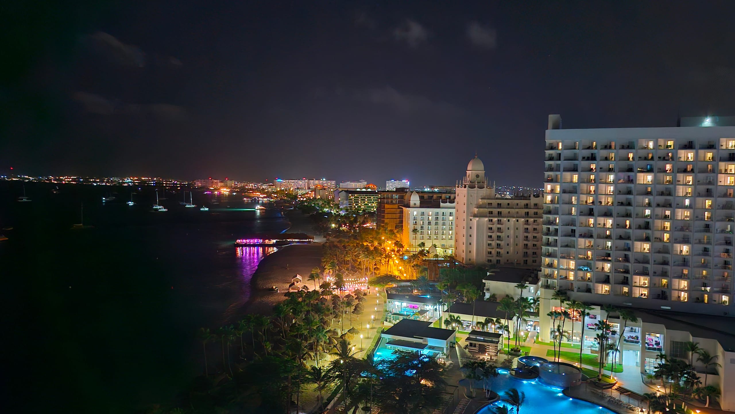 Palm Beach hotels lit up at night in Aruba, the shoreline and a lit pier curving away toward more hotel towers