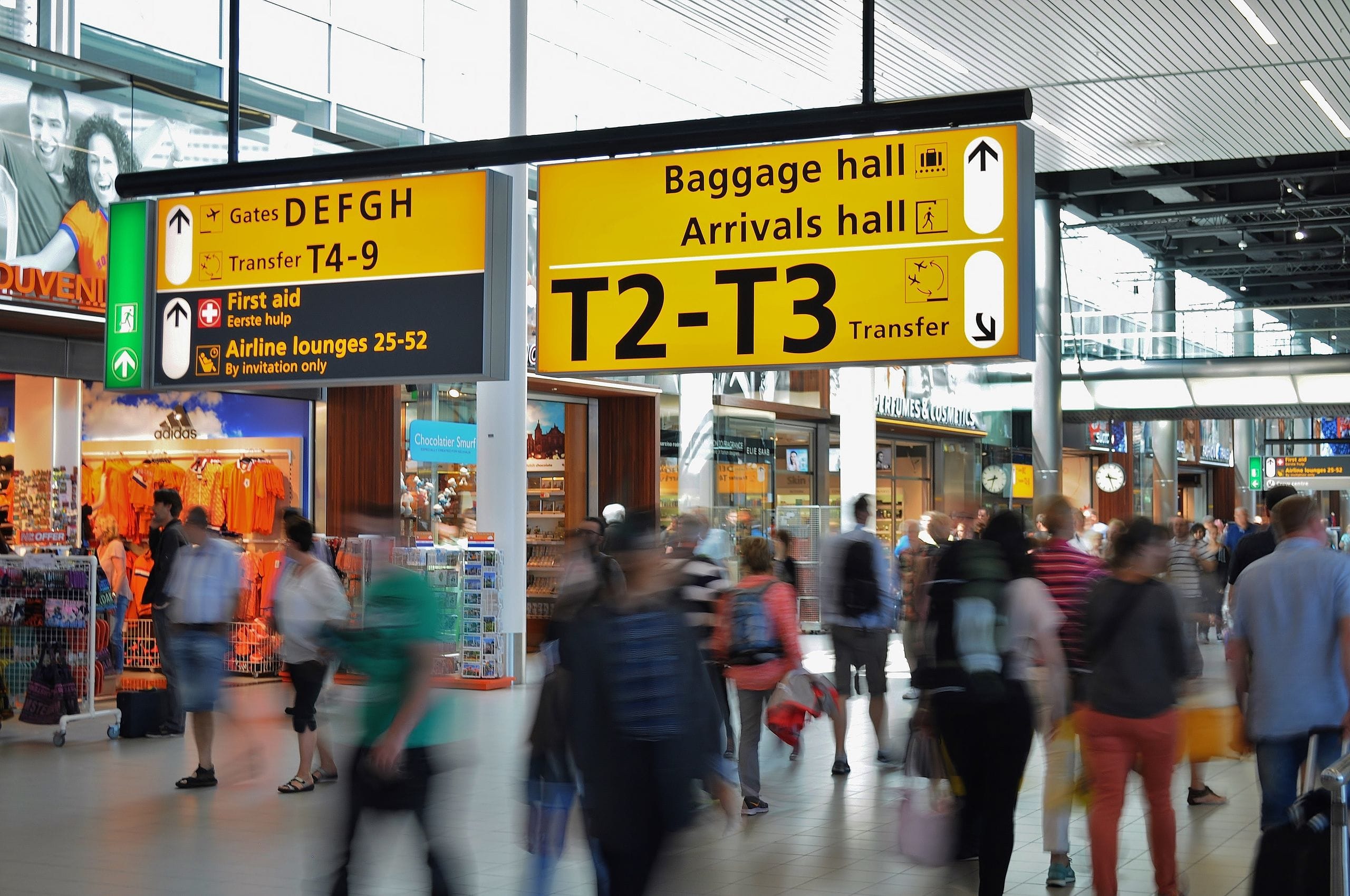 Yellow airport signs pointing to the baggage hall and arrivals hall above a crowd of passengers with bags