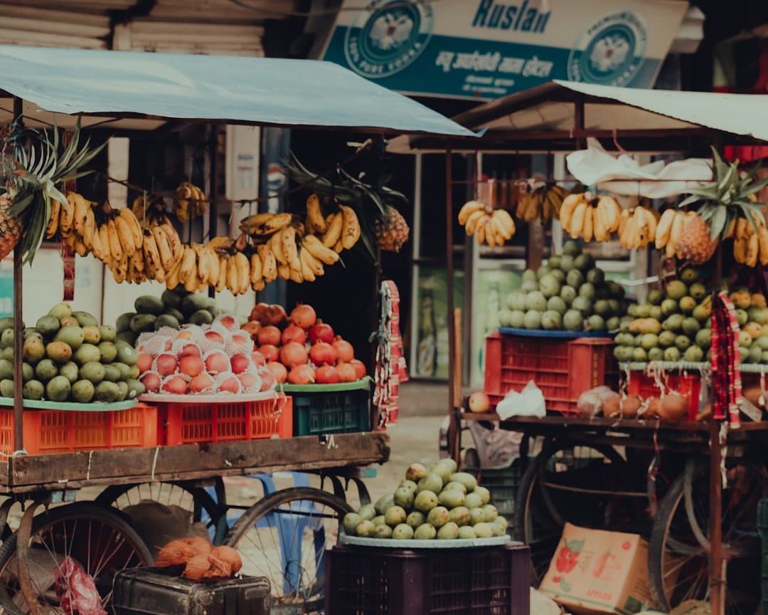 Fruit carts at a roadside market in Butwal, Nepal, bunches of bananas hanging above crates of apples and other fruit