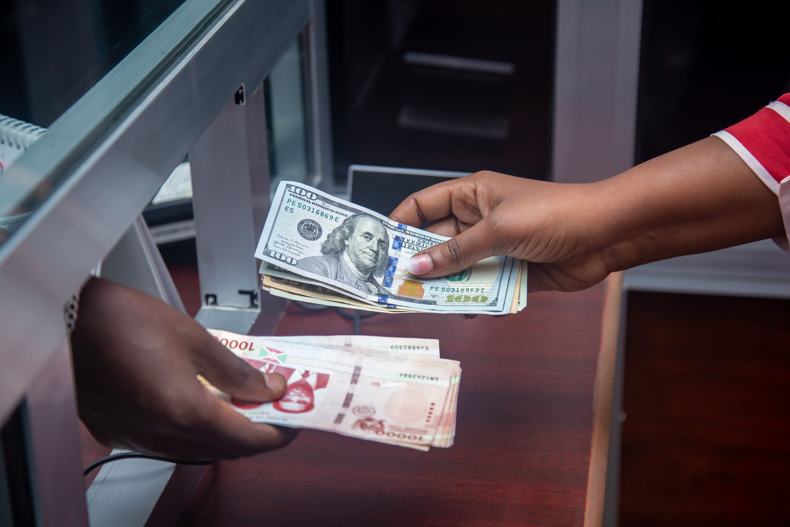 Two hands trading a stack of US hundred-dollar bills for a stack of local banknotes at a counter