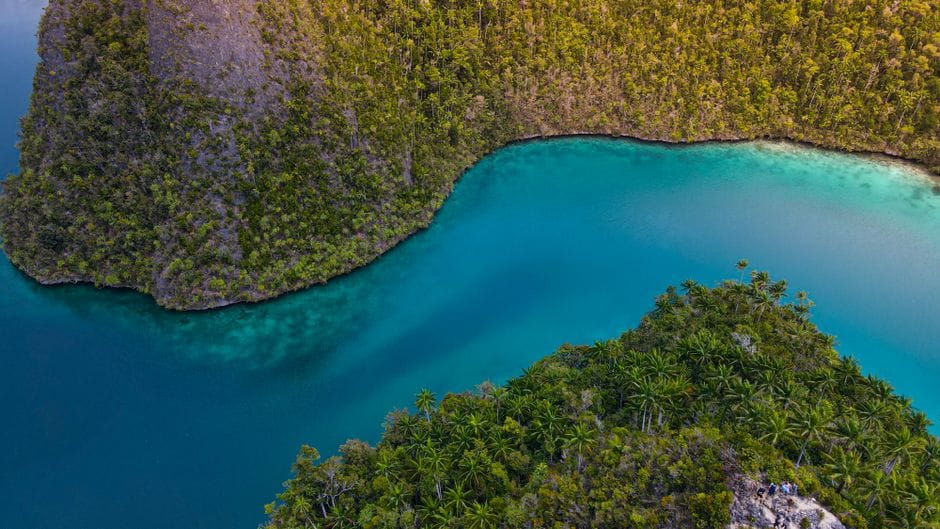 A turquoise lagoon curving around a green tropical island seen from above