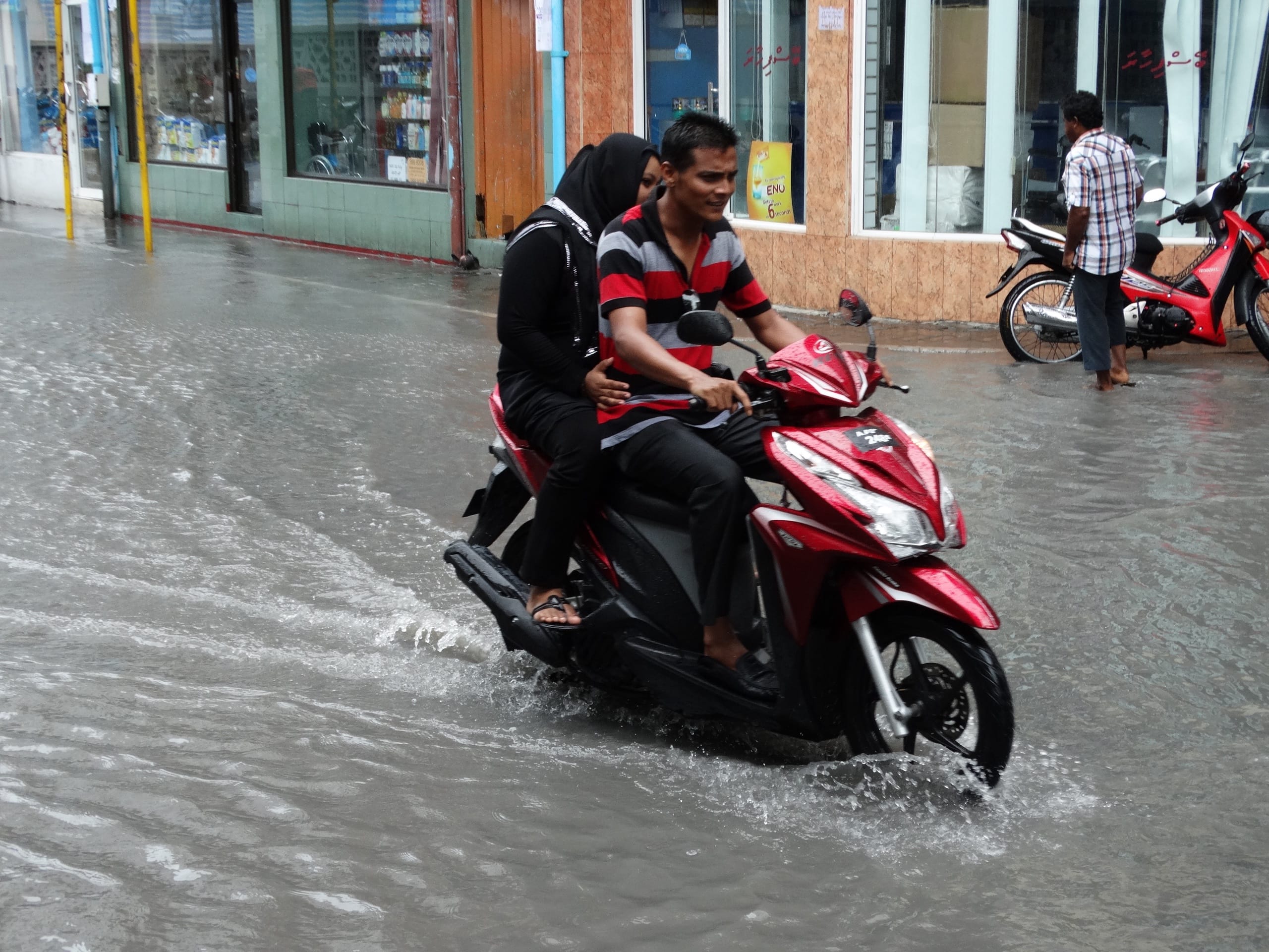 A couple on a red scooter ride through a flooded street in Malé after heavy rain