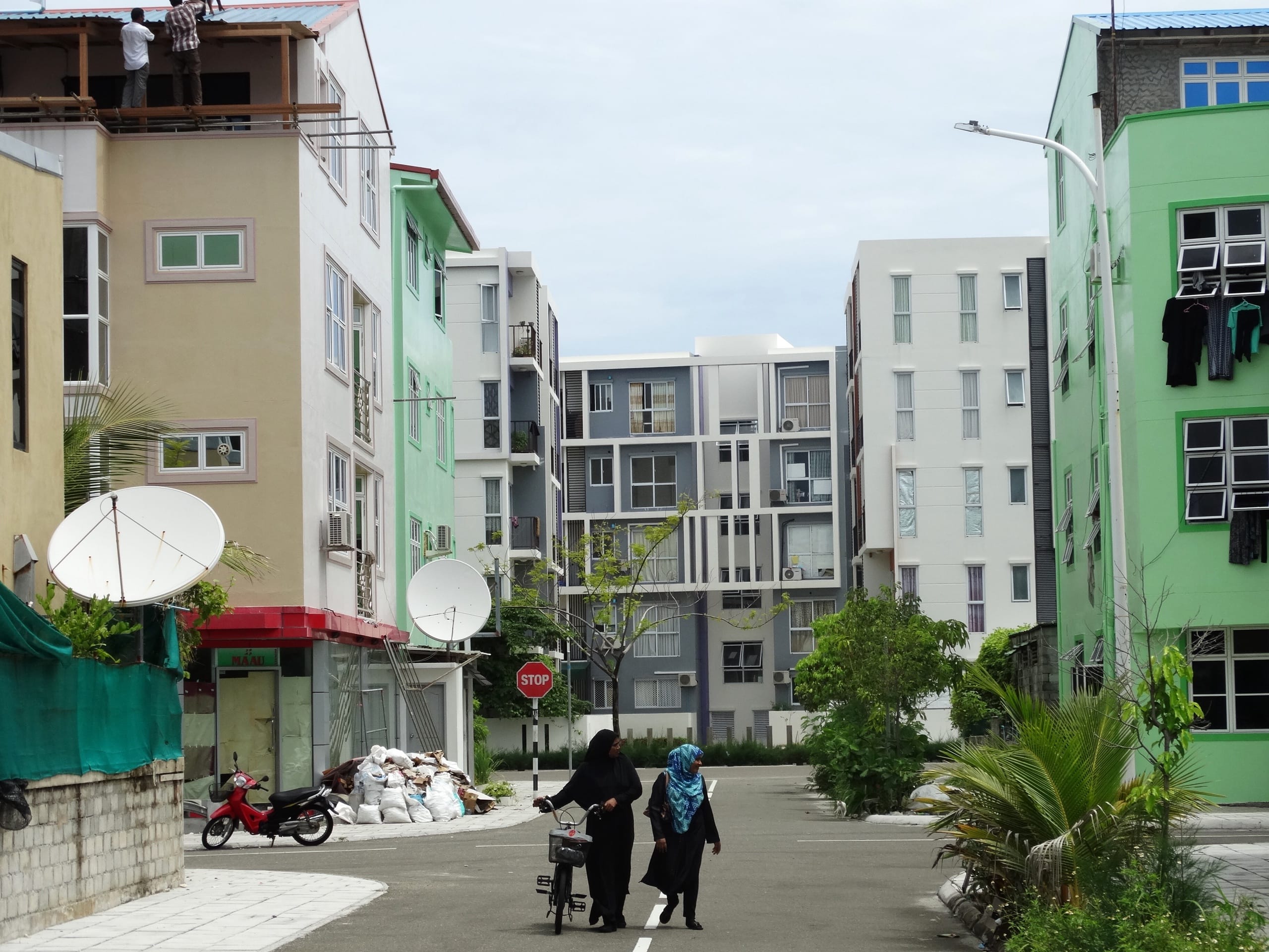 A quiet street in Hulhumalé lined with colorful apartment blocks, two women walking and a red scooter parked