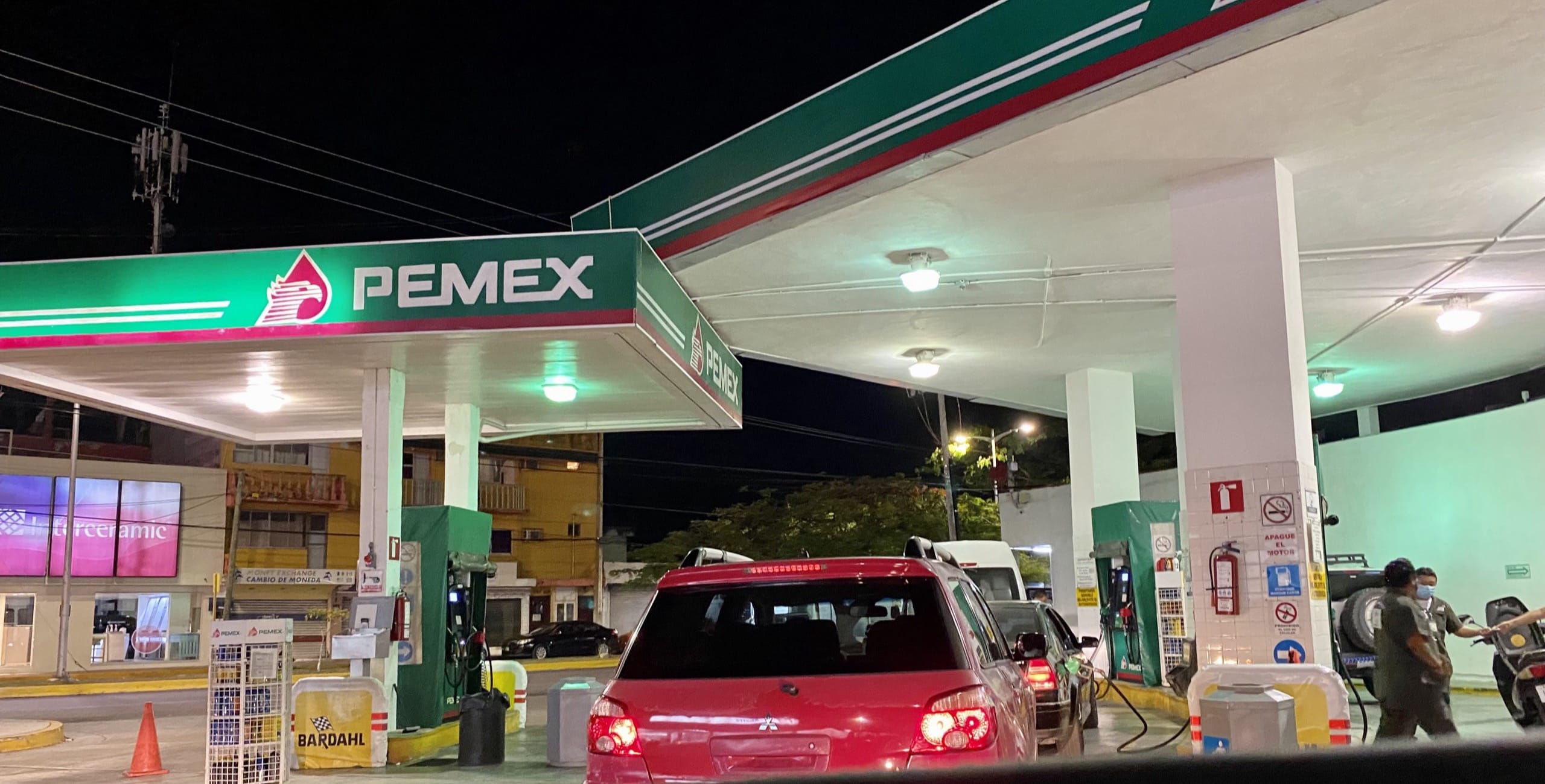 Pemex station at night with a red car waiting at the pump and attendants working the forecourt
