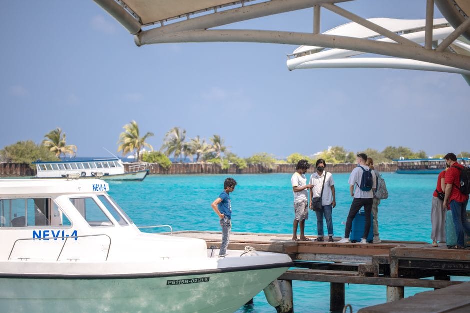 Travelers standing on a jetty in the Maldives under a shade canopy, a speedboat tied up alongside