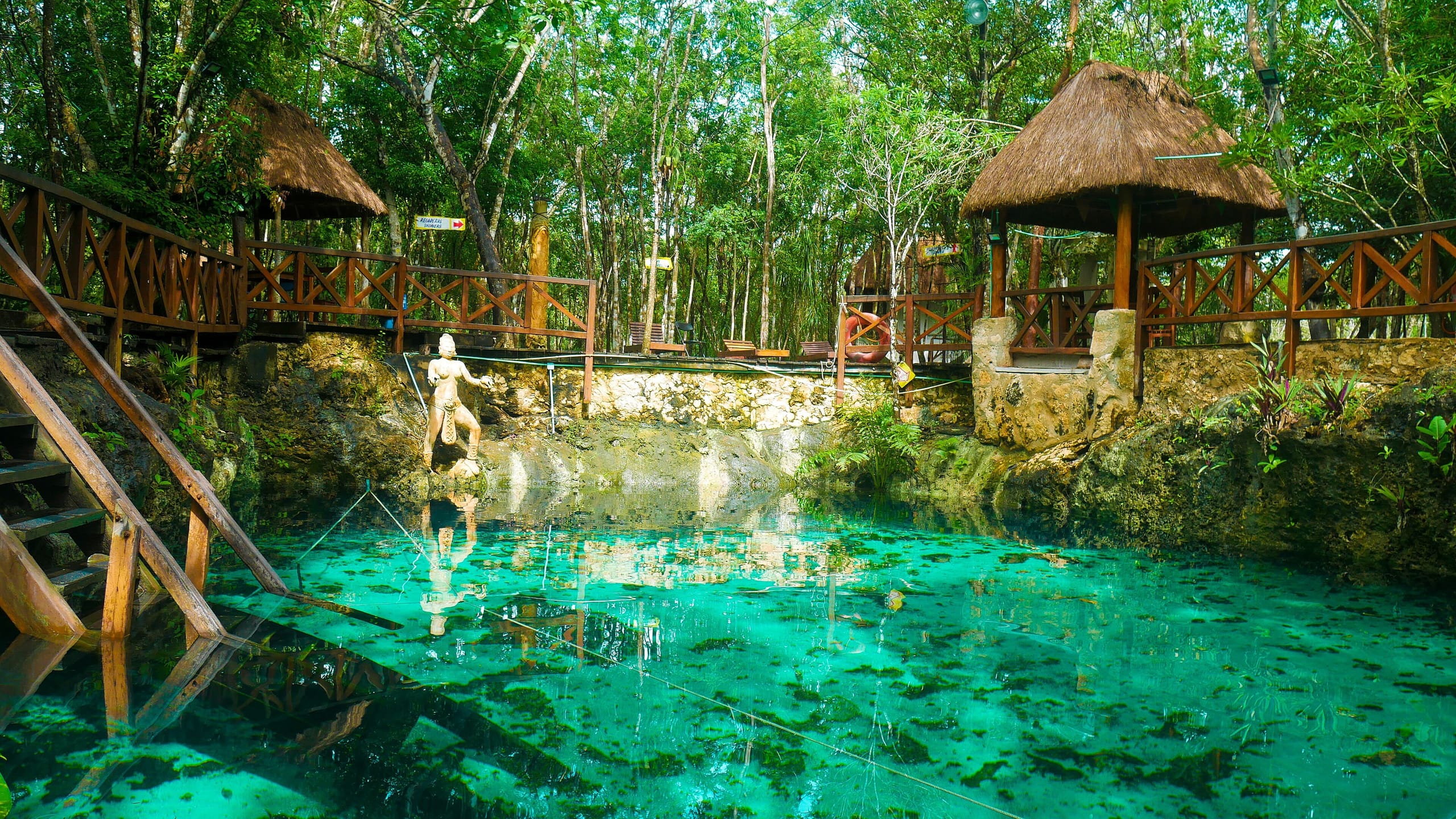 Cenote Zacil-Ha's open turquoise pool with thatched palapas and wooden railings around it
