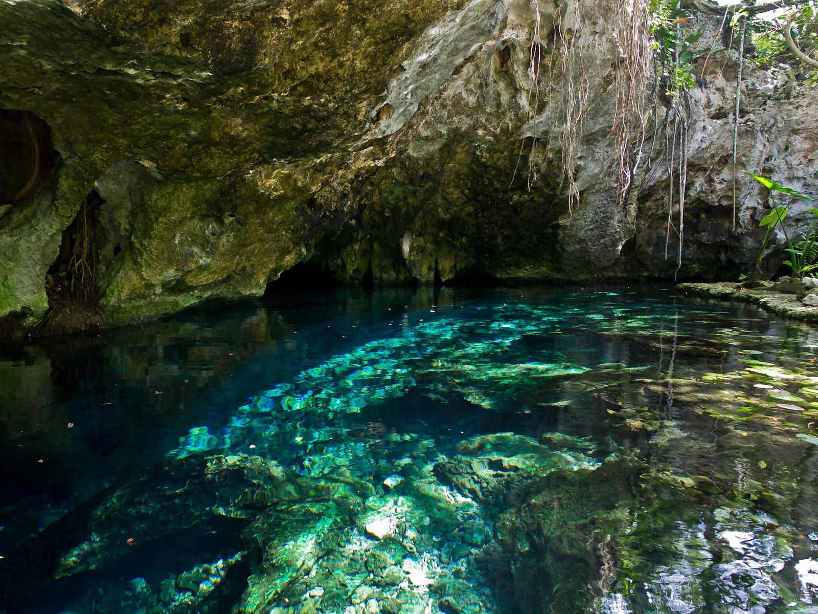 The low rock passage and clear blue water at Gran Cenote, with daylight at the far end