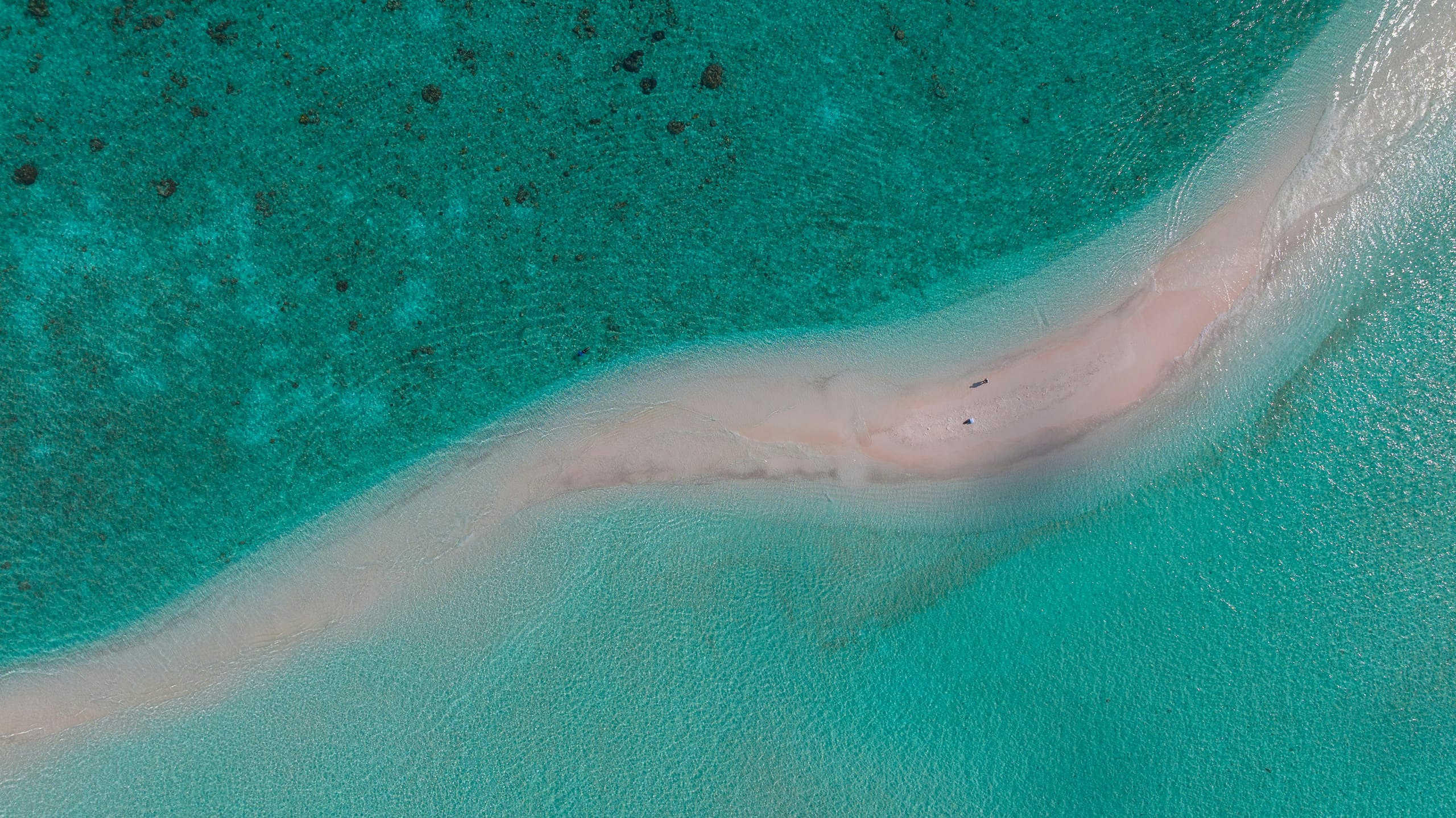 A white sandbar curving through turquoise water seen from above