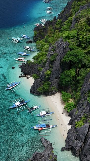 Outrigger boats along a rocky tree-covered shoreline in Coron, Palawan, seen from the air