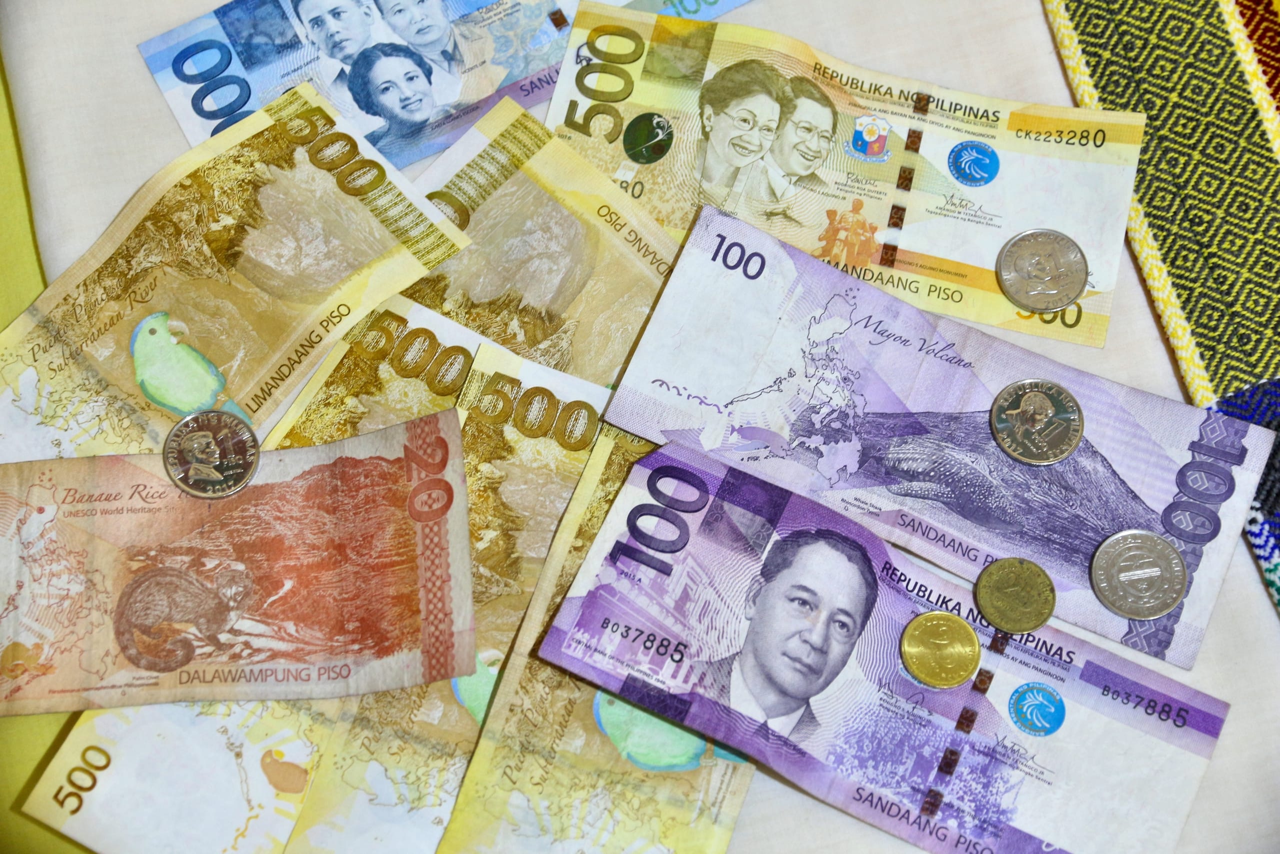 Philippine peso banknotes in several denominations scattered with coins on a cream cloth