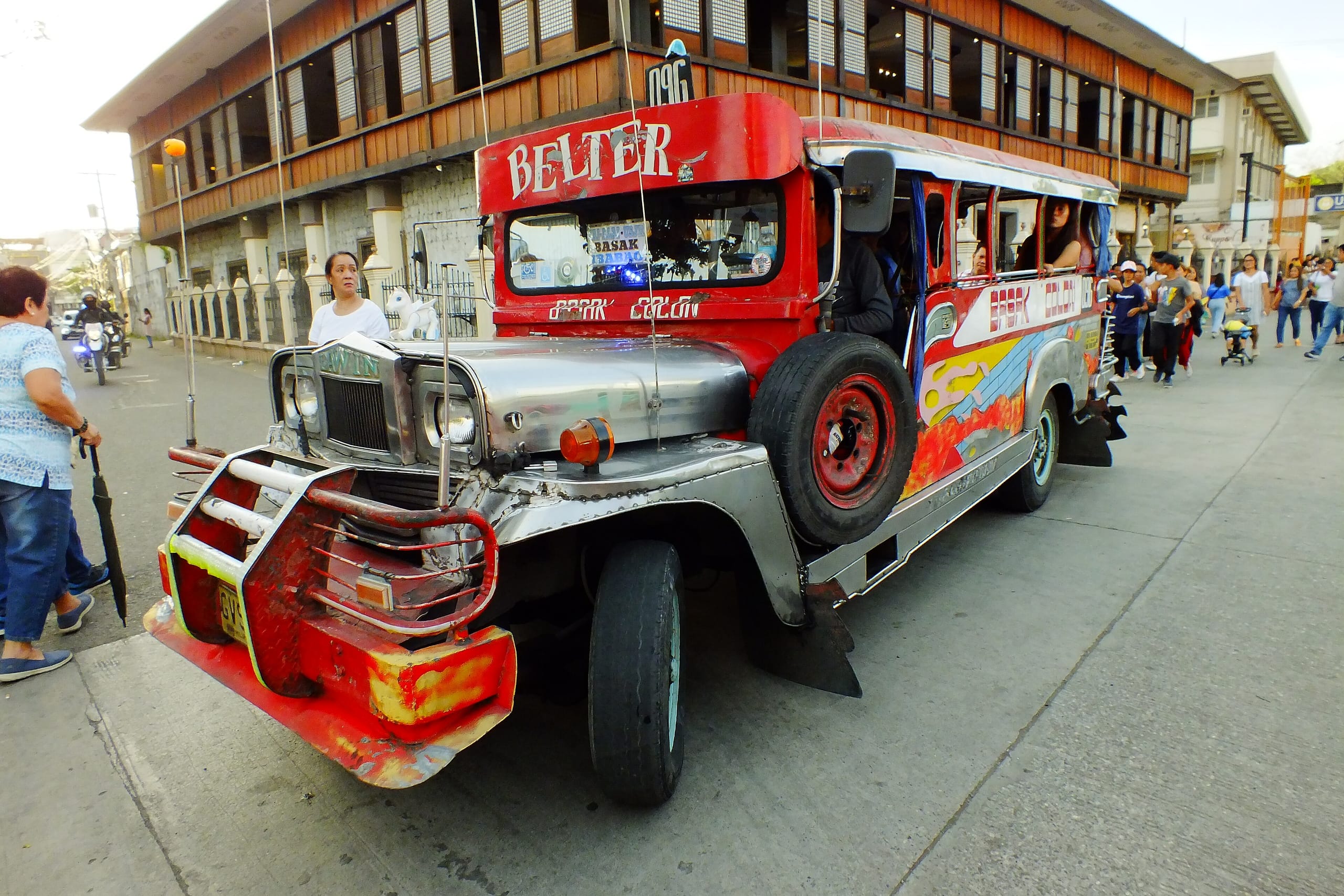 Red painted jeepney with a spare tire on its flank turning through a busy Cebu City street