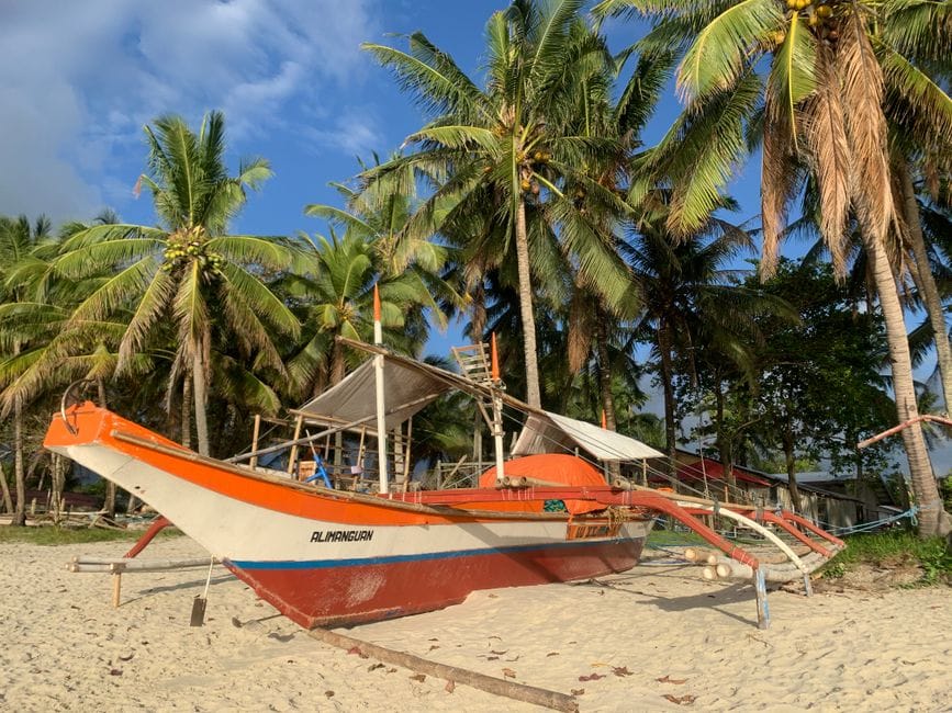 An outrigger boat hauled up on the sand under coconut palms at San Vicente, its name painted along the bow