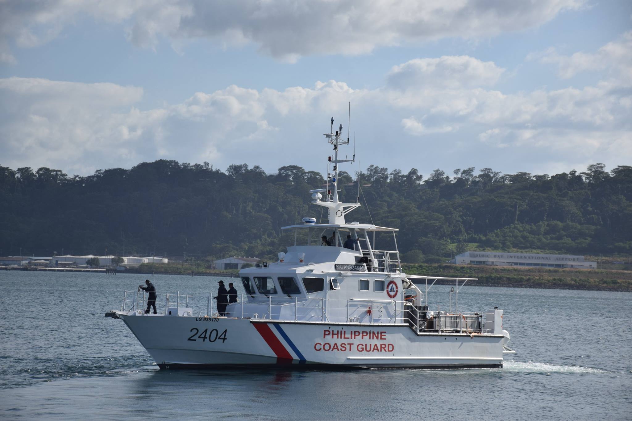 Philippine Coast Guard fast patrol boat with number 2404 underway in a bay, wooded hills behind it