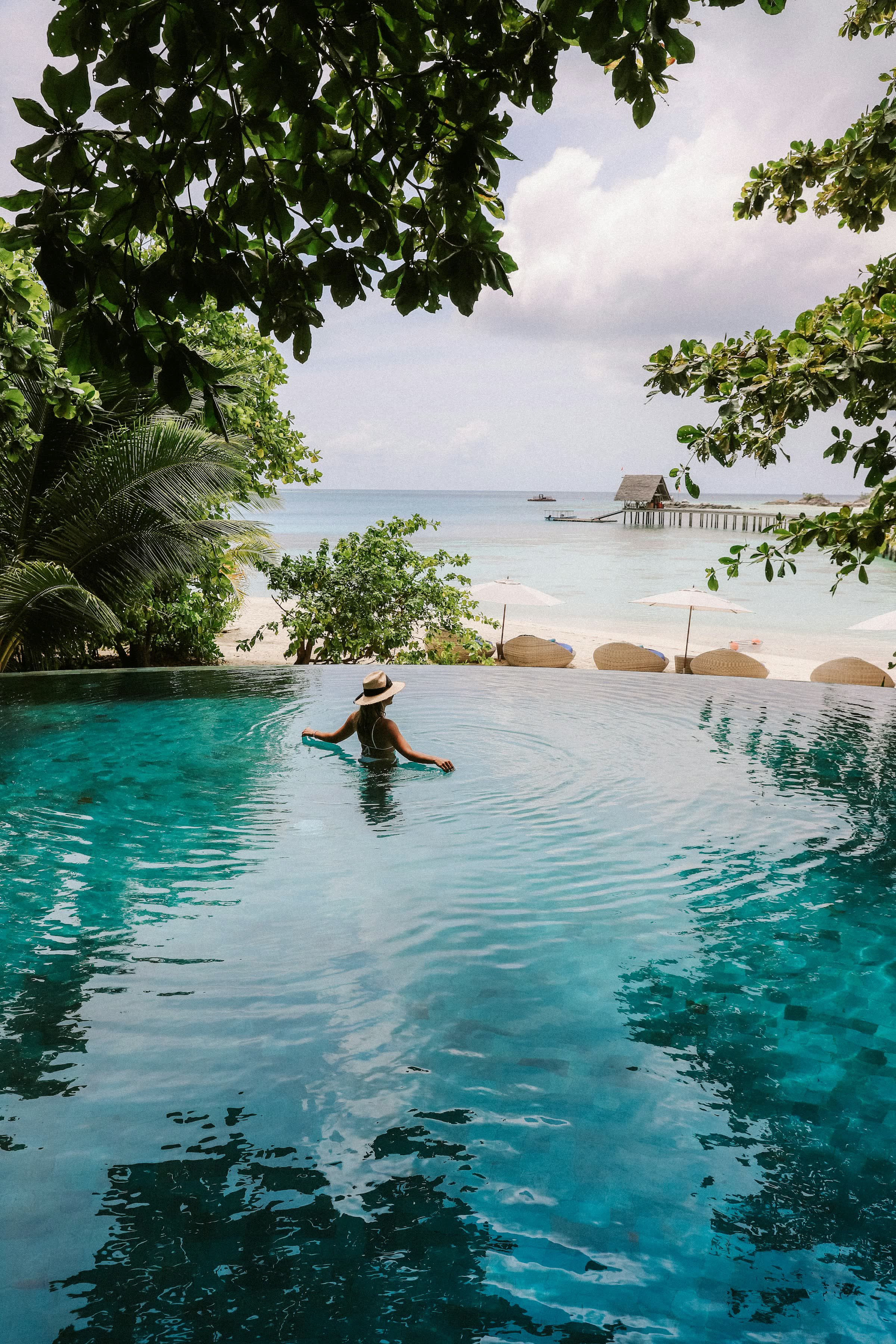 An infinity pool looking out through beach foliage toward a jetty and the open lagoon
