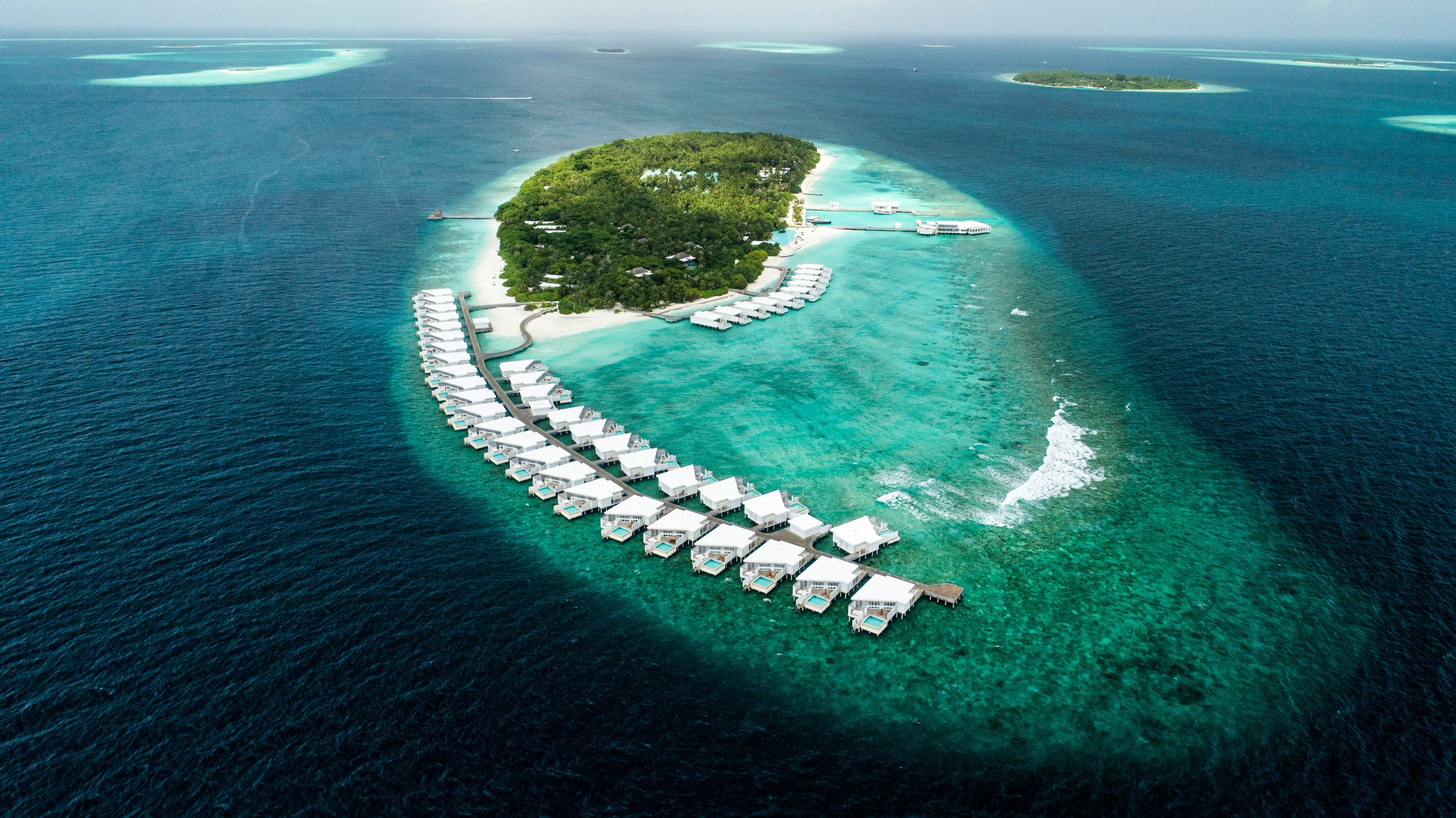 An oval island ringed by a continuous line of white overwater villas in deep blue water